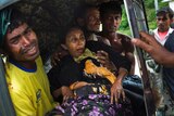 An injured elderly woman, who appears to be in great pain, held by her male relatives on an autorickshaw.