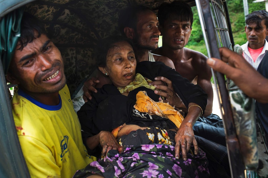 An injured elderly woman, who appears to be in great pain, held by her male relatives on an autorickshaw.