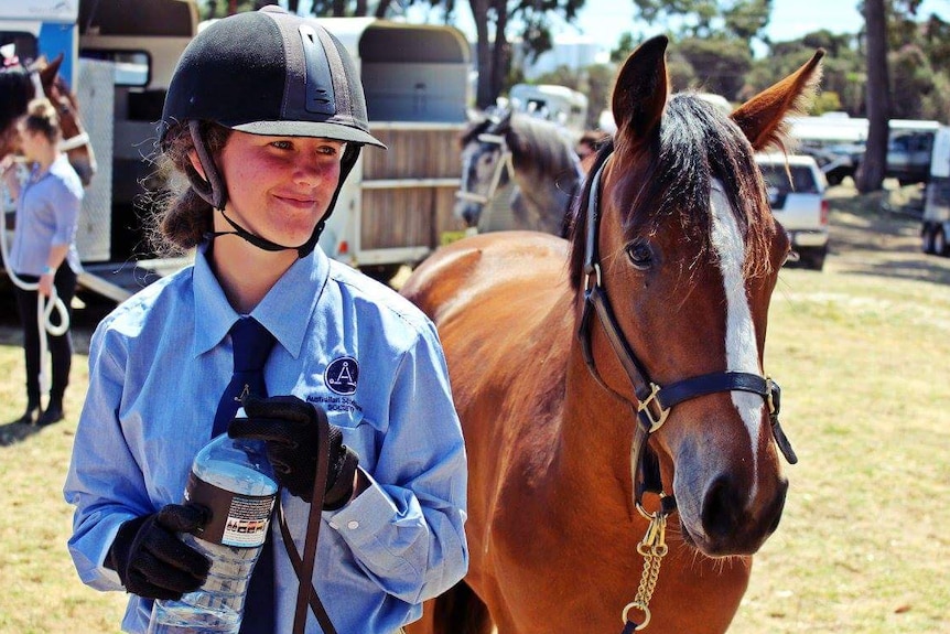 Alexandra Henderson pictured wearing horse riding gear and standing next to a horse.
