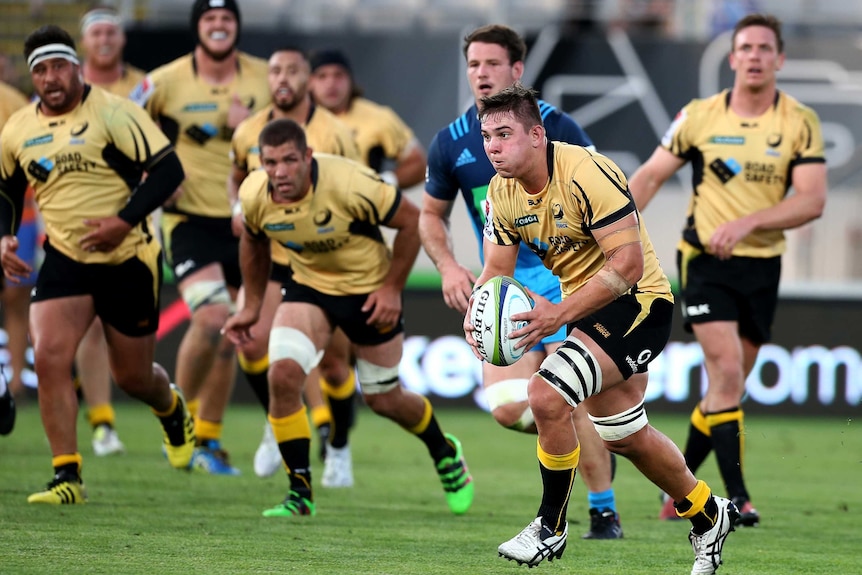 Richard Hardwick prepares to pass a rugby ball wearing the Western Force's yellow away jersey, with other players behind him.