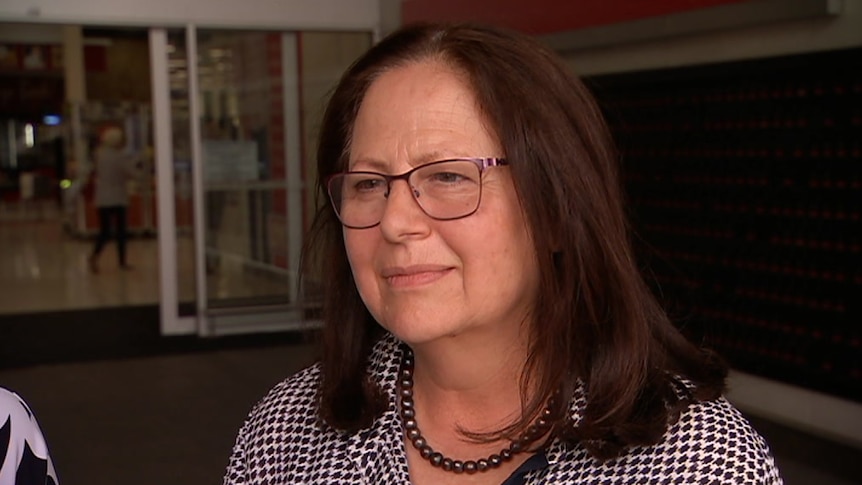 A brunette woman wearing glasses standing in front of a shopping centre