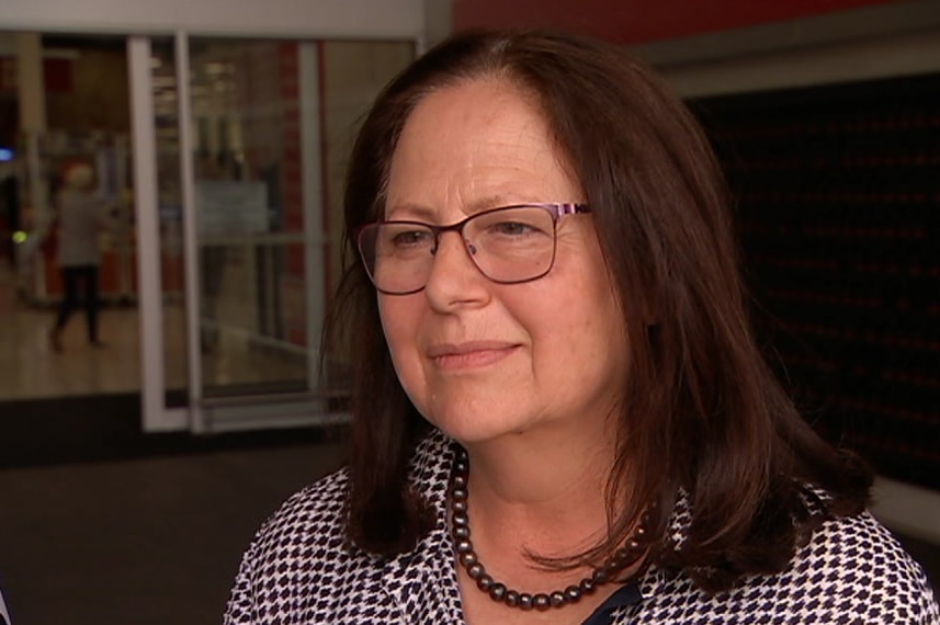 A brunette woman wearing glasses standing in front of a shopping centre