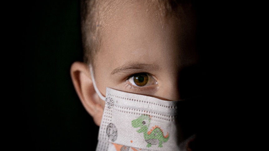 Child's face wearing a face mask and half obscured by darkness