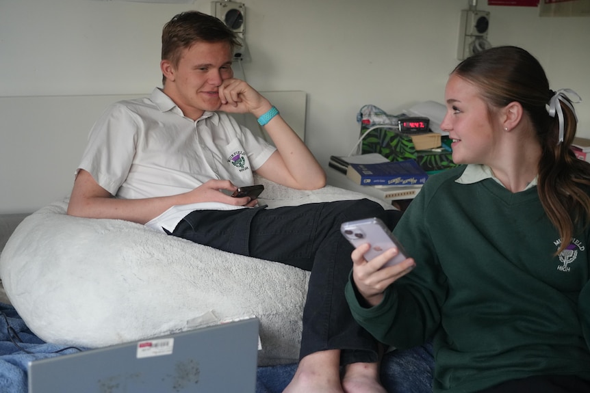 A teenage boy and girl sit in a room conversing.