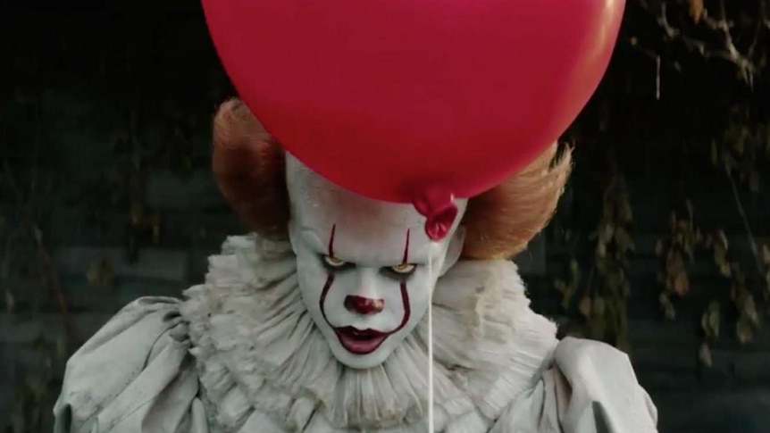 Still image of Bill Skarsgård as Pennywise, a supernatural villainous clown holding a red balloon in 2017 film IT.
