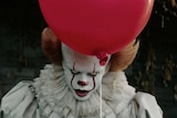 Still image of Bill Skarsgård as Pennywise, a supernatural villainous clown holding a red balloon in 2017 film IT.