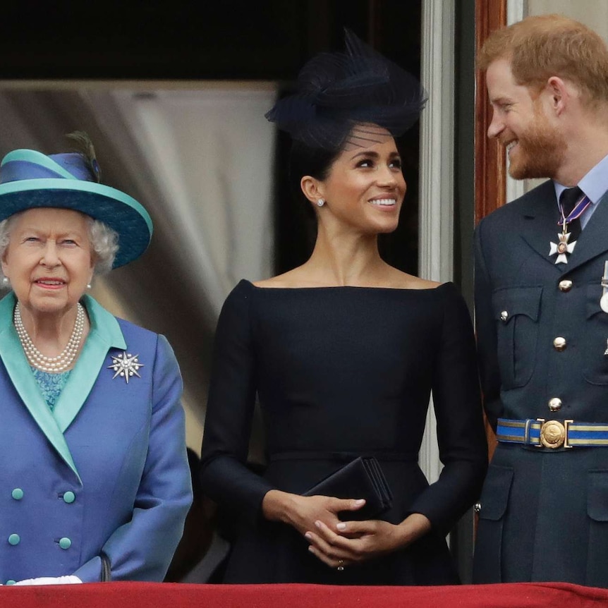 Queen Elizabeth II stands on a balcony, while Harry and Meghan, Duke and Duchess of Sussex, look at each other.