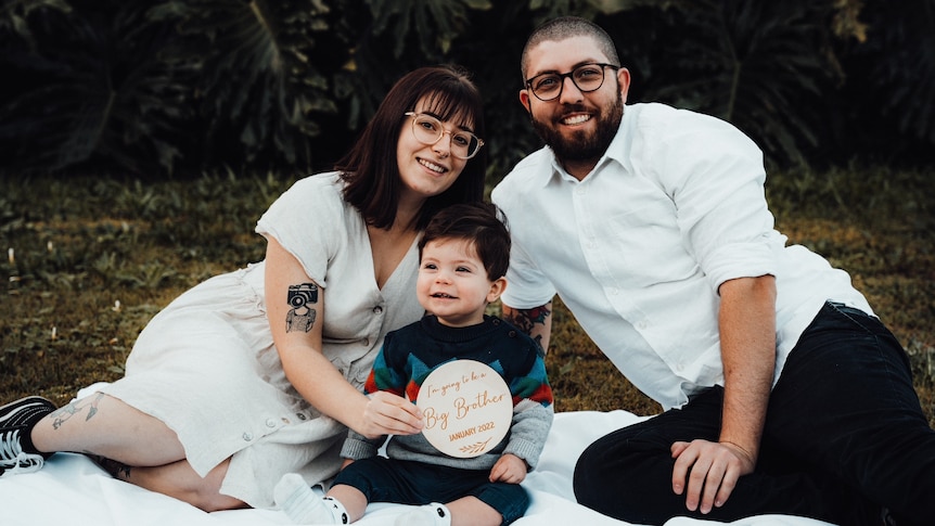 a woman posing for a family photo with partner and small child