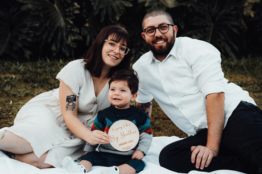 a woman posing for a family photo with partner and small child