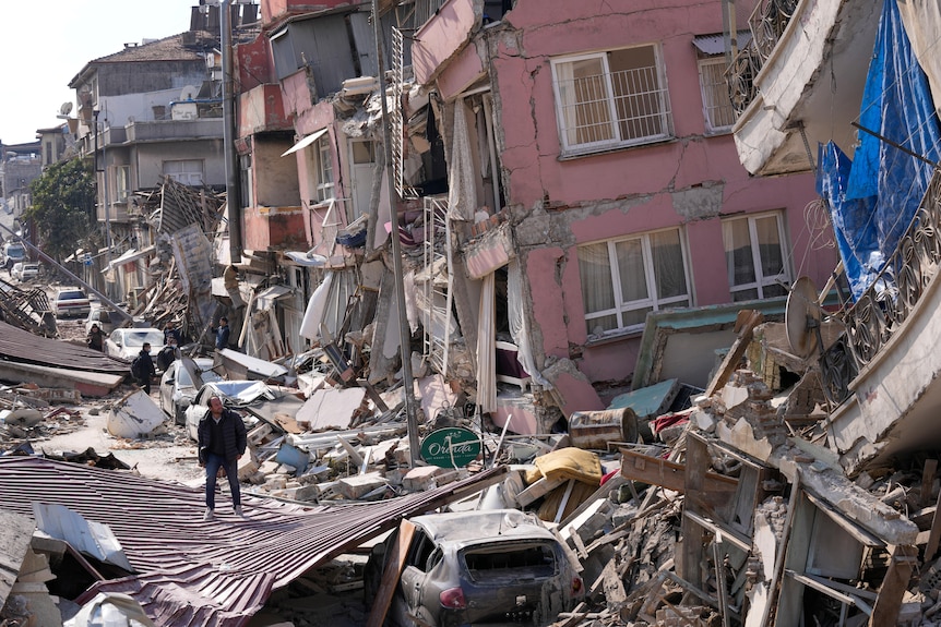 A man walks over debris of collapsed buildings.
