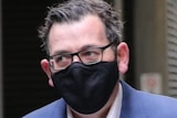 Daniel Andrews is shown wearing a dark-coloured face bask as he arrives for a press conference.