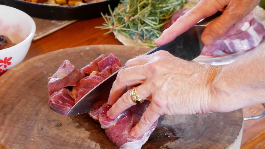 A close up and a woman cutting meat on a chopping board with a knife.