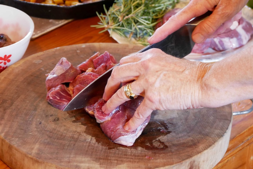 A close up and a woman cutting meat on a chopping board with a knife.