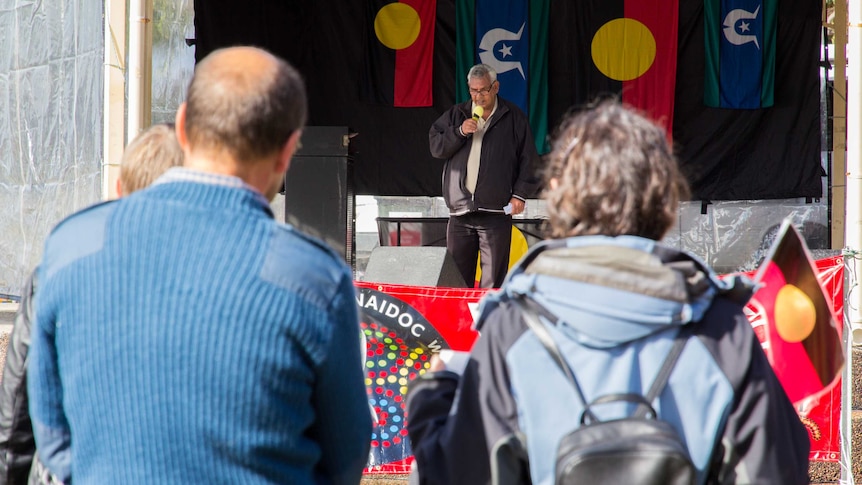 Two people watch a speaker at a NAIDOC Week event in Toronto.