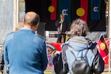 Two people watch a speaker at a NAIDOC Week event in Toronto.