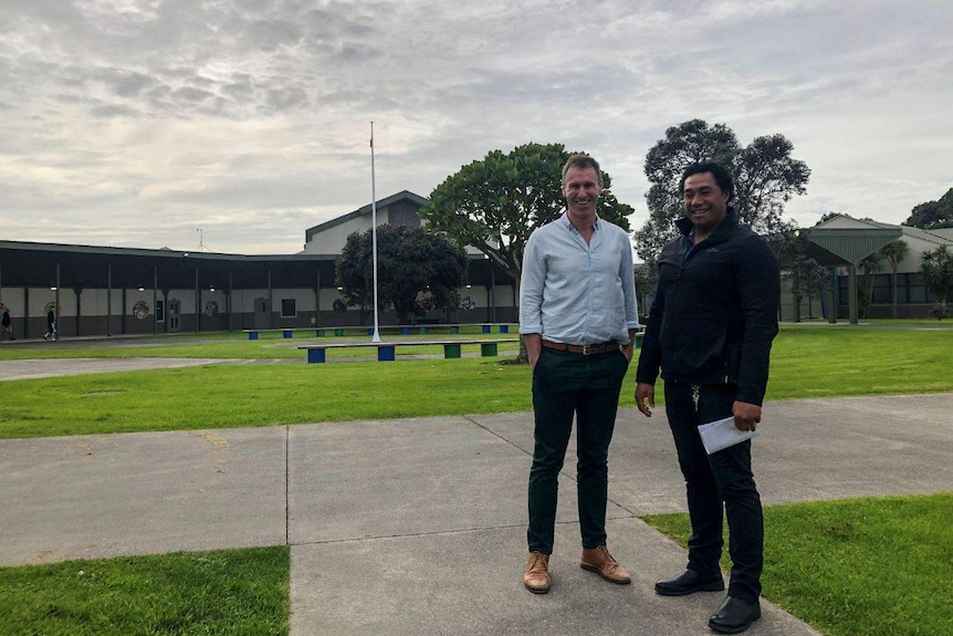 Two men stand side by side in an open courtyard.