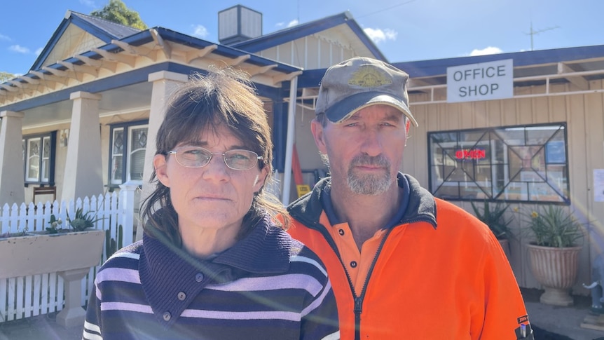 Two middle-aged people standing in front of a caravan park and looking stern.