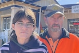 Two middle-aged people standing in front of a caravan park and looking stern.