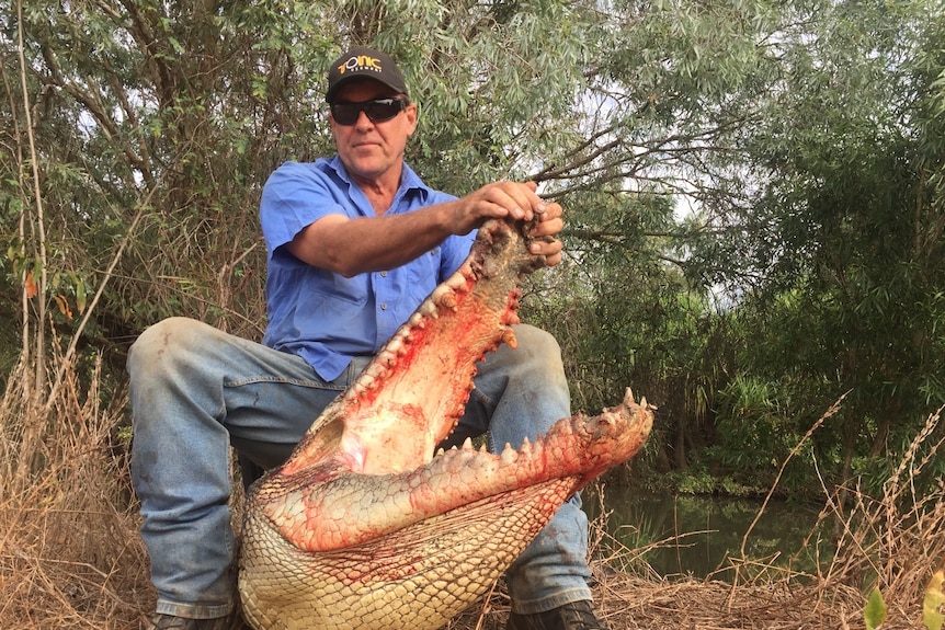 A man sits on top of a crocodile that he's caught. 