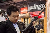 A man holds a gun with a Remington sign in the background.