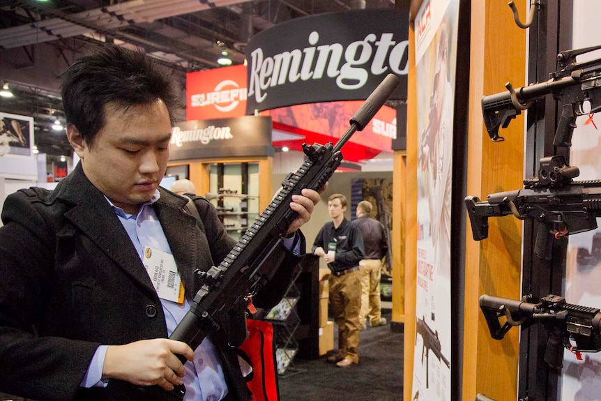 A man holds a gun with a Remington sign in the background.