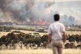 Fire in the background with a man standing looking on