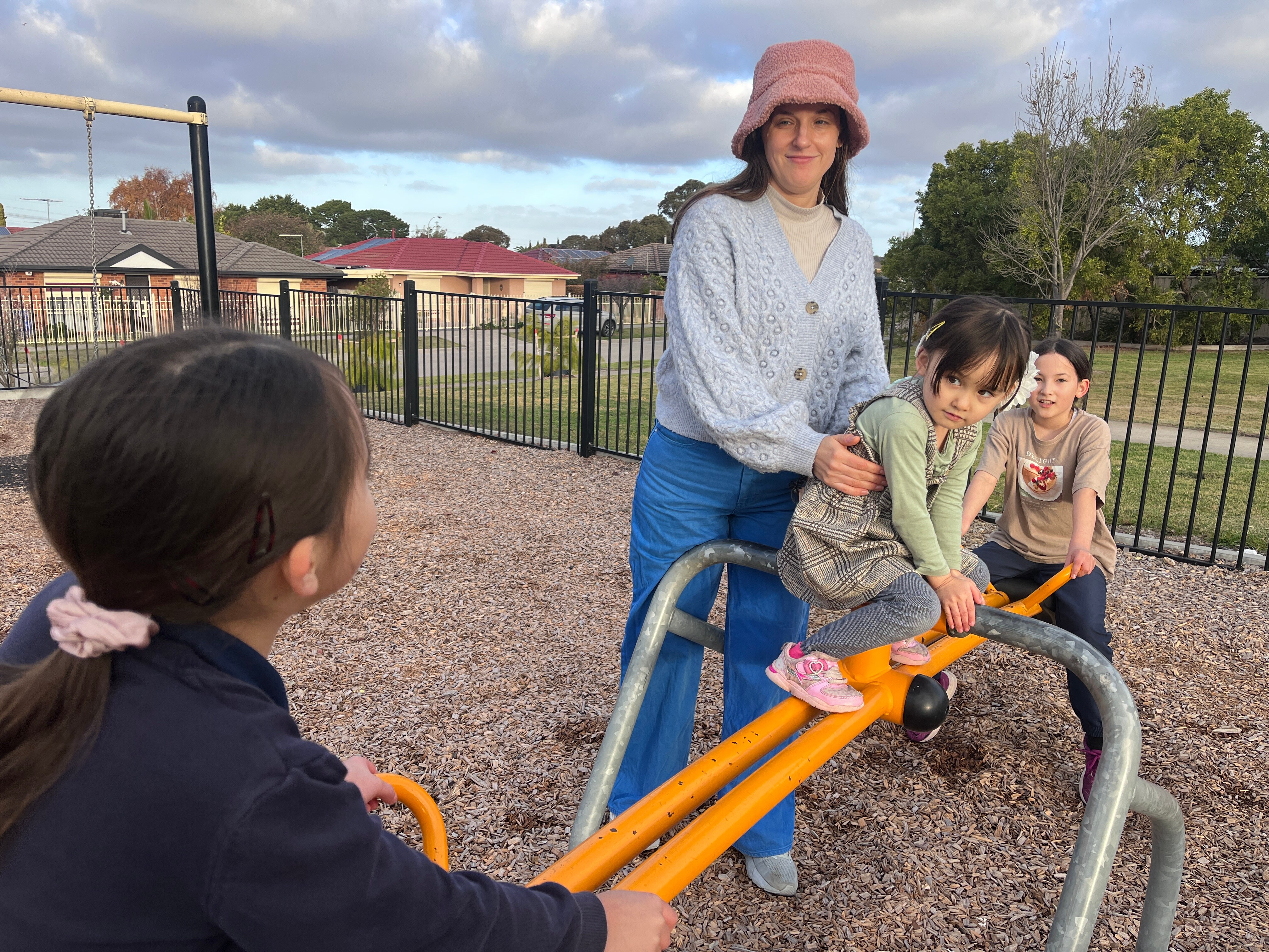 Una madre con sus tres hijos pequeños en un patio de recreo.