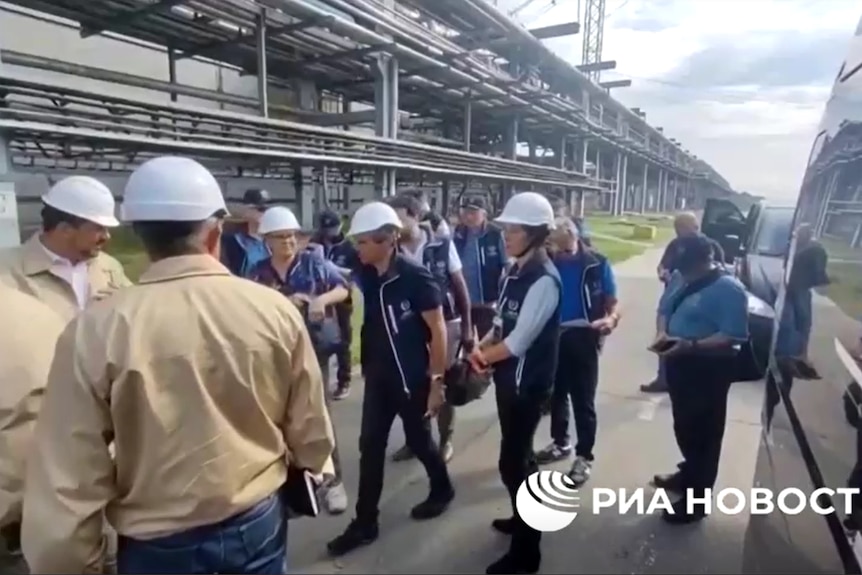 IAEA officials in navy vets wear white helmets as they are shown around a nuclear power plant.