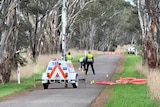 Crash site investigators stand on a quiet rural road.