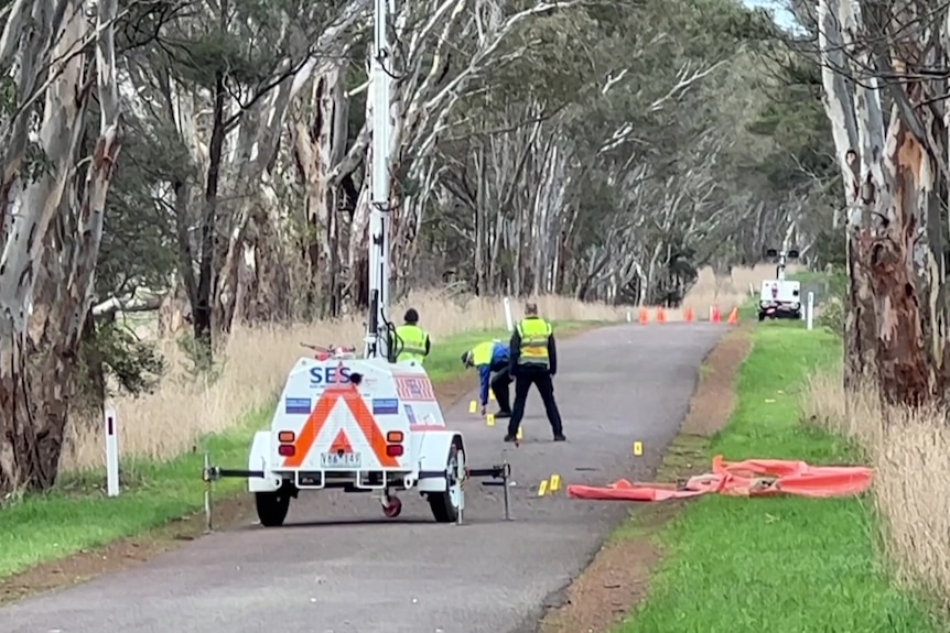 Crash site investigators stand on a quiet rural road.