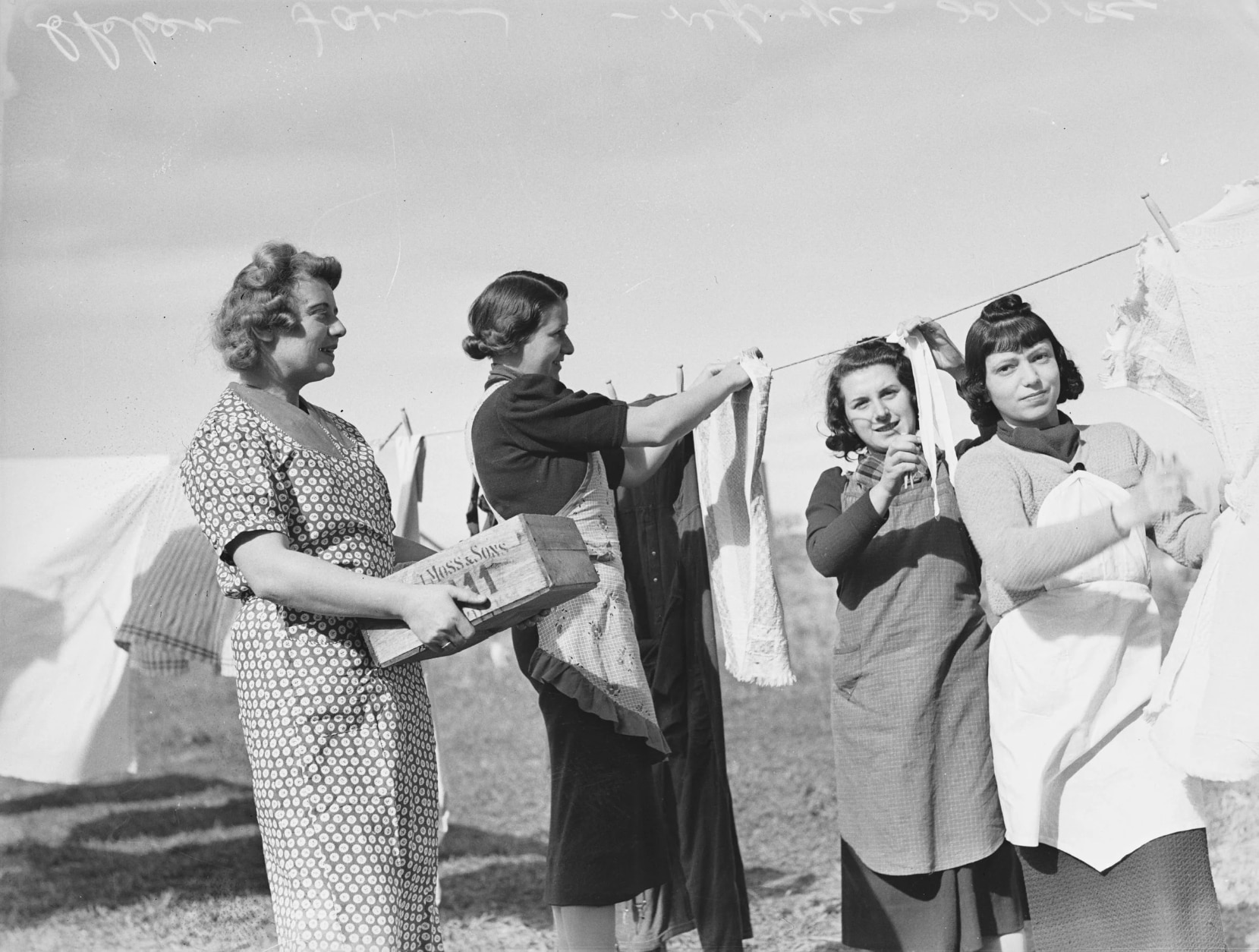 An archival black and white photo of four jewish women doing laundry tasks on a clothing line.