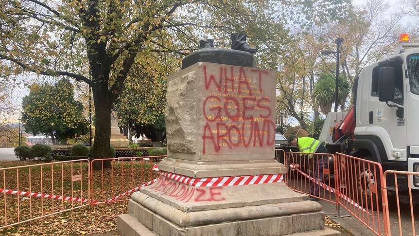 A sandstone plinth with red graffiti saying 'What goes around".