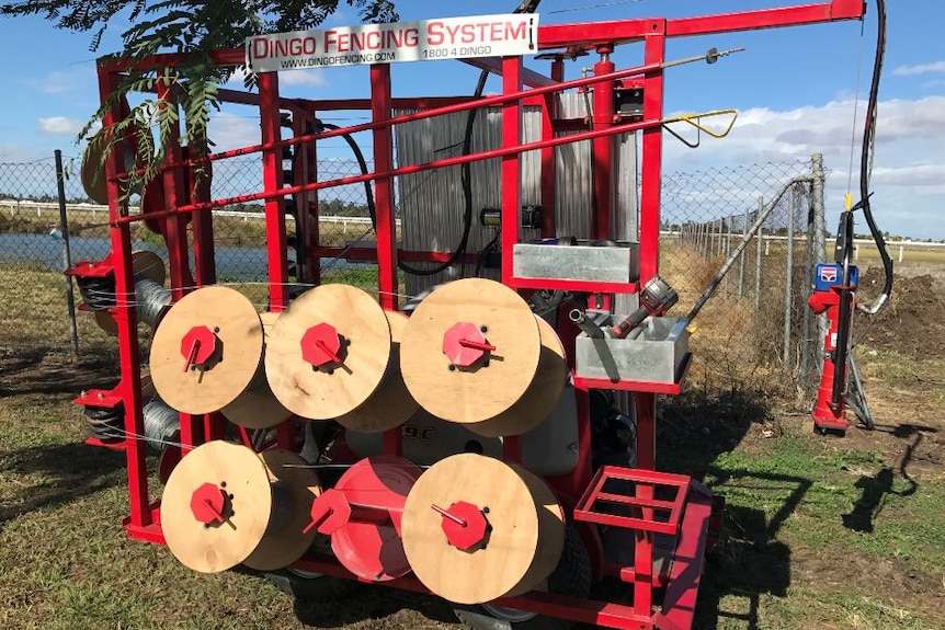 A large red machine with fencing reeled around wheels.