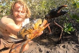A man covered in mud holding a crab.