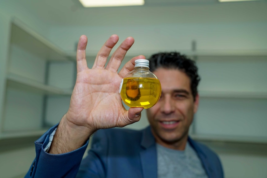 A man holding up a bottle of yellow liquid