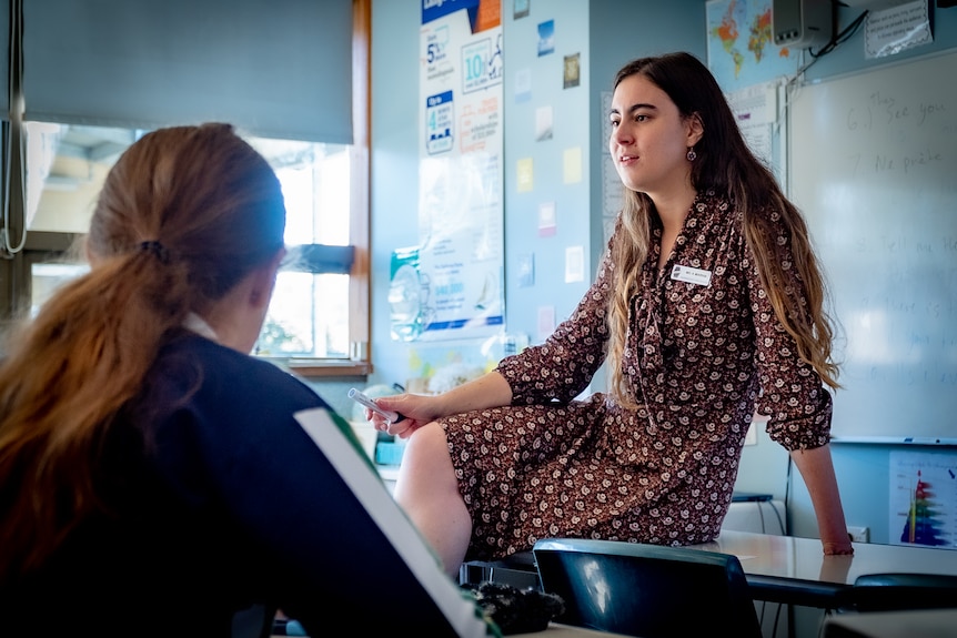 Ayelet Marha sitting on a desk leaning on her hand, speaking to a class.