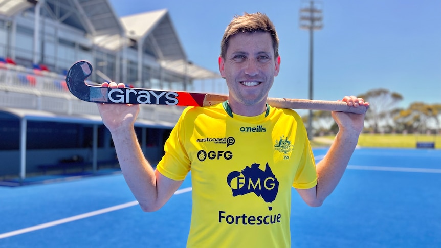 A man wearing a yellow shirt holding a hockey stick on a blue court