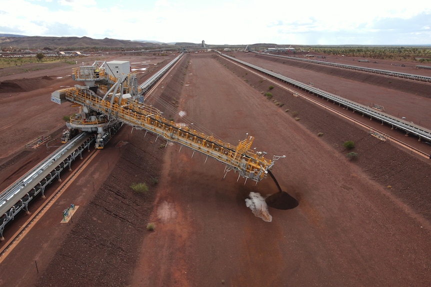 A crane pours out red dirt into a long rectangular hole.