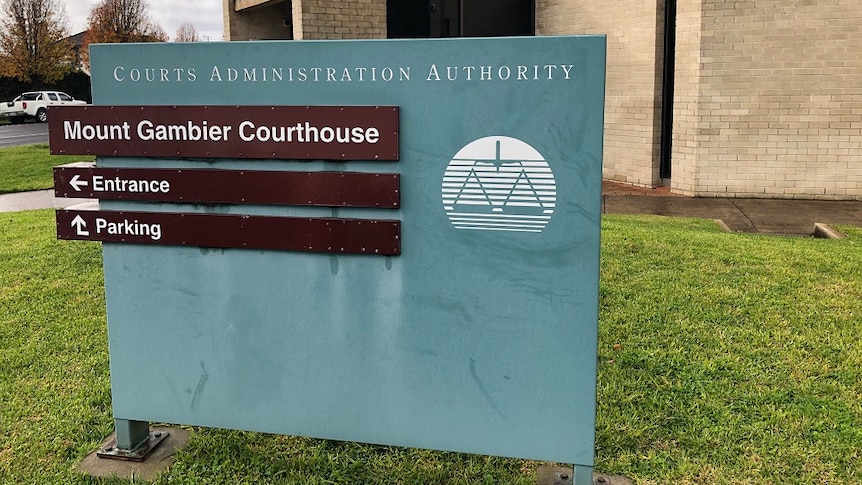 A blue sign in front of a brick building, reading "Court Administration Authority, Mount Gambier Courthouse, Entrance, Parking"