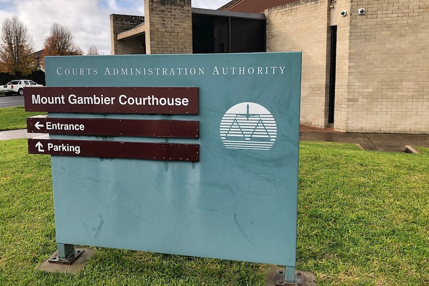 A blue sign in front of a brick building, reading "Court Administration Authority, Mount Gambier Courthouse, Entrance, Parking"