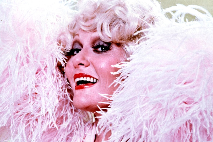 Jeanne Little wears a bright pink feather boa while she wears red lipstick and lashes