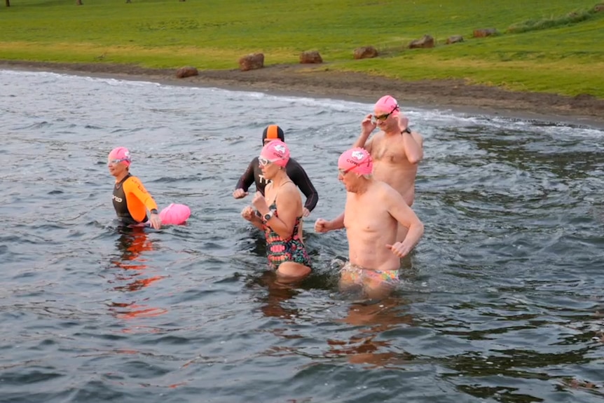 Very cold swimmers in bathers walk slowly into a large cold lake
