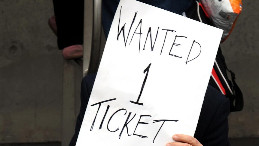 A person wanting tickets holds a sign outside a venue