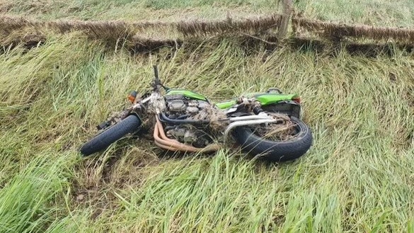  A green bike on its side in grass near a fence.