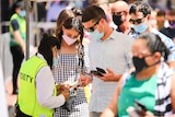 A man and a woman wearing masks show a security guard their phones.
