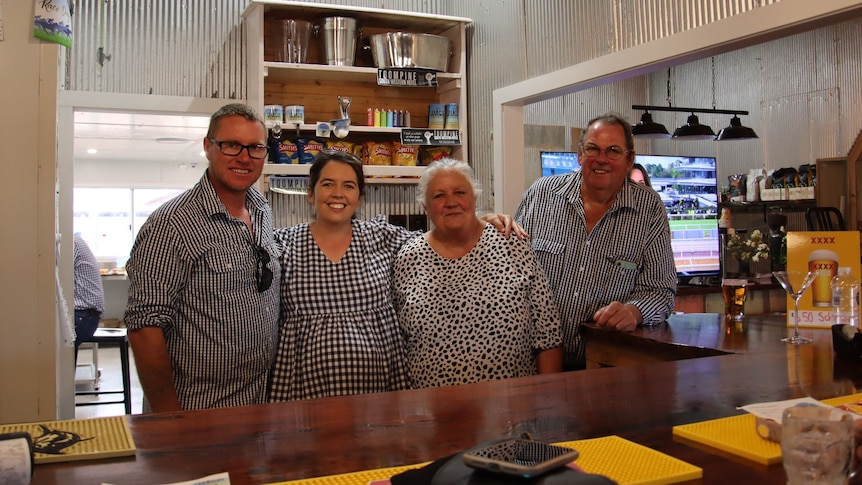 Two men and two women stand behind a wooden bar in a pub. All smiling.