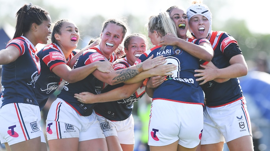 Sydney Roosters players gather and smile in celebration