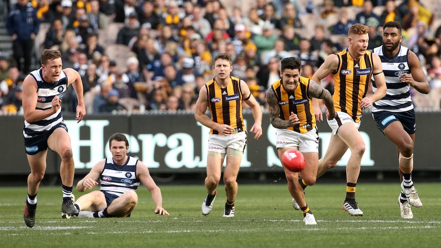 An AFL player races after the ball while his opponents are left trailing or sitting on the ground.