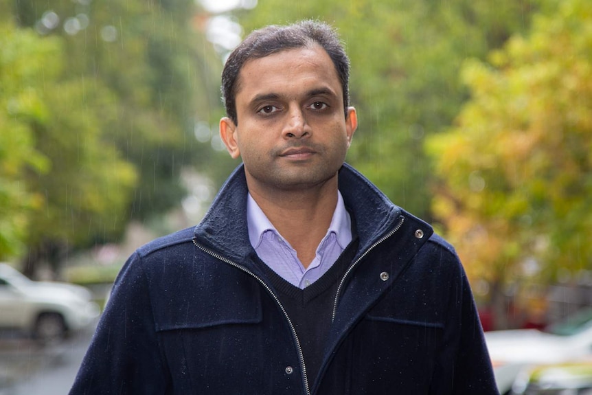 A man wearing a navy blue coat stands in the rain.