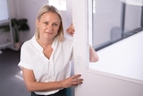 A woman in a white shirt smiles next to a door.
